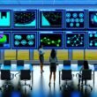 Data-Operations-Raum mit mehreren Bildschirmen, Marketingexperten analysieren Live-Daten, Charts und Workflow-Diagramme in modernem Ambiente.