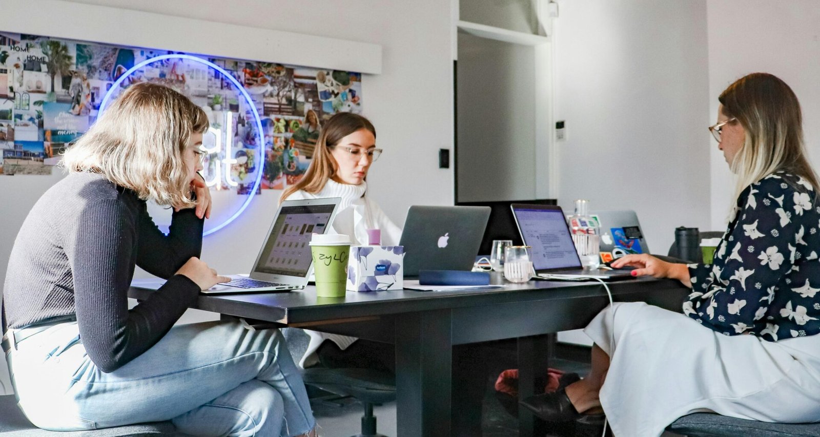 Drei Frauen sitzen an einem Tisch mit Laptops und arbeiten gemeinsam an einem Projekt in einem modernen Büro.