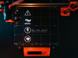 Nahaufnahme einer 3D-Drucker-Bauplattform mit klaren Warnsymbolen zur Anzeige potenzieller Gefahrenbereiche