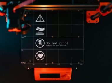 Nahaufnahme einer 3D-Drucker-Bauplattform mit klaren Warnsymbolen zur Anzeige potenzieller Gefahrenbereiche