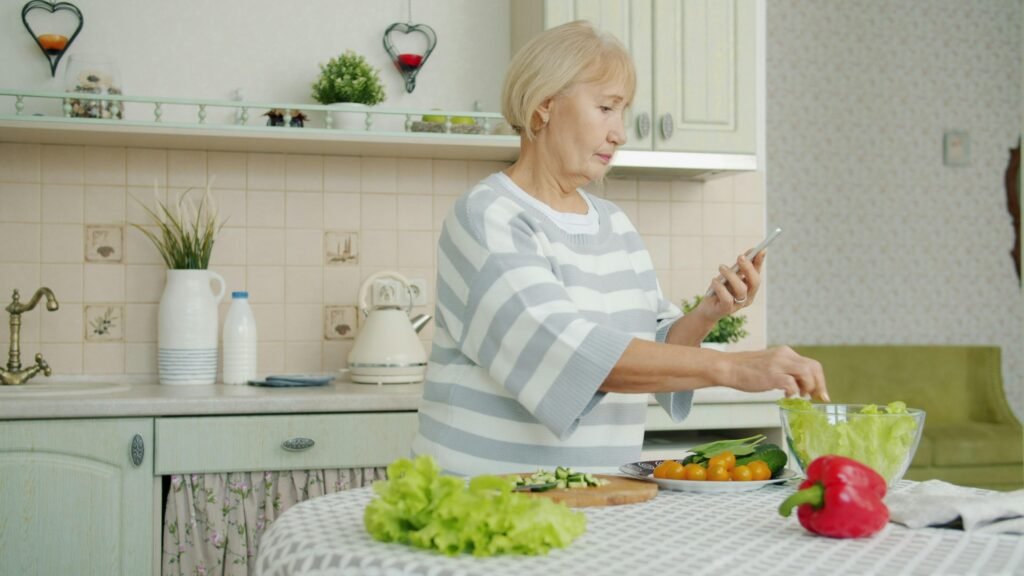 Ältere Frau steht in einer modernen Küche und bereitet aus frischen Zutaten einen gemischten Salat zu