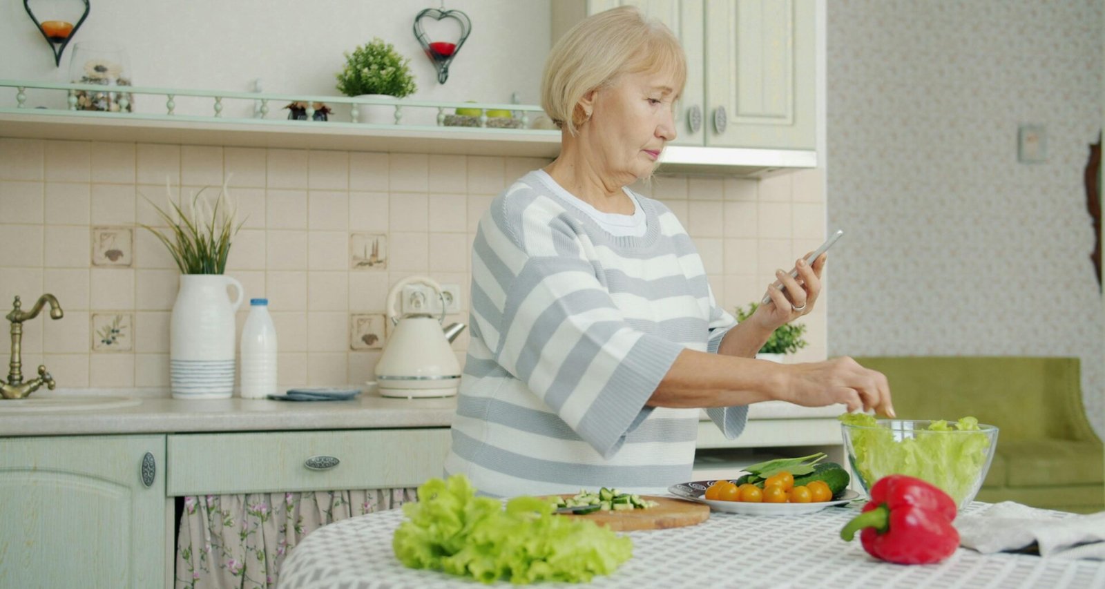 Ältere Frau steht in einer modernen Küche und bereitet aus frischen Zutaten einen gemischten Salat zu