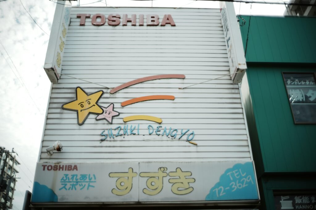 Altes Toshiba Schild mit Cartoon-Sternen und japanischen Schriftzeichen auf rostigem Metall, aufgenommen bei Tageslicht