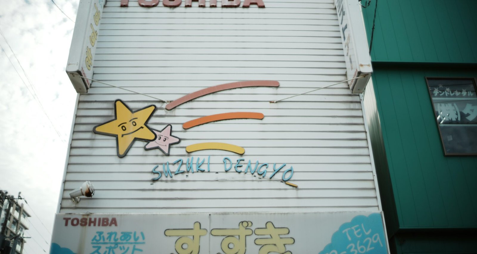 Altes Toshiba Schild mit Cartoon-Sternen und japanischen Schriftzeichen auf rostigem Metall, aufgenommen bei Tageslicht