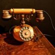 Ein antikes, schwarzes Wählscheibentelefon steht auf einem dunklen, hölzernen Tisch. Aufnahme von Cansu Sarp.