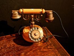 Ein antikes, schwarzes Wählscheibentelefon steht auf einem dunklen, hölzernen Tisch. Aufnahme von Cansu Sarp.