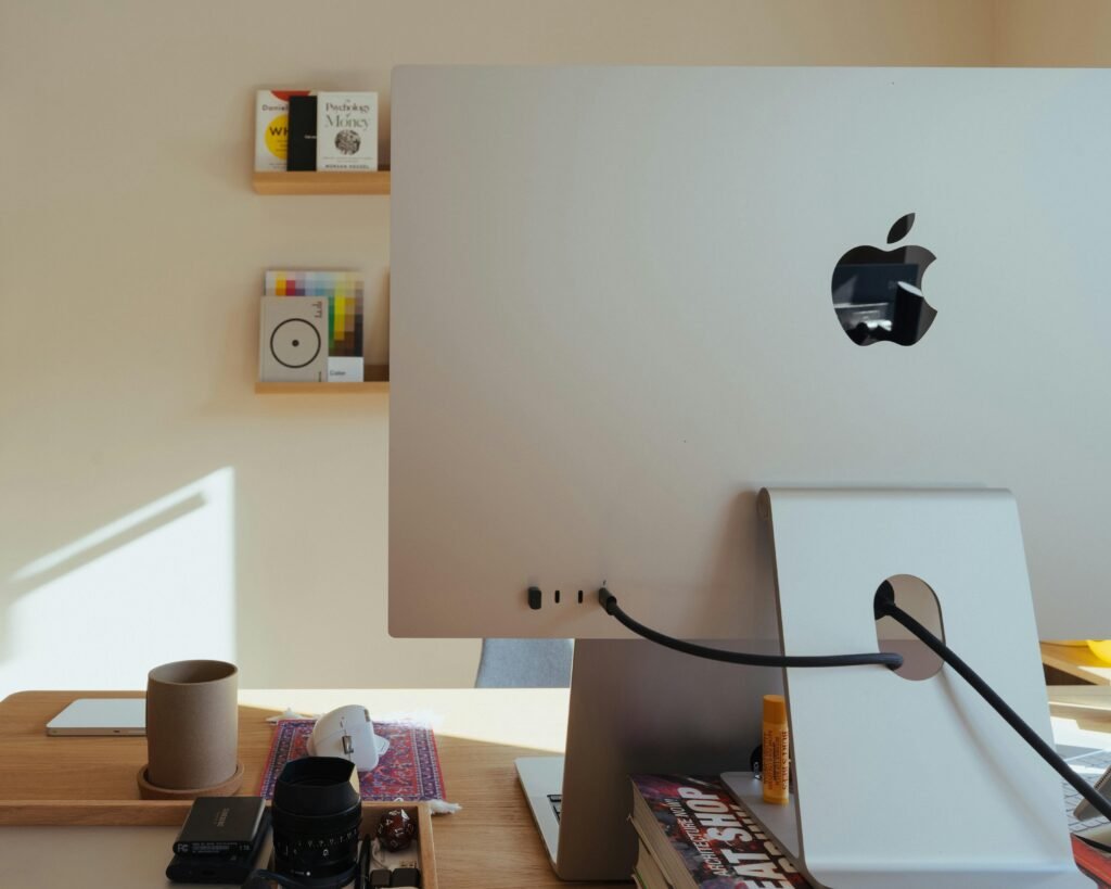 Apple Computer steht auf einem Schreibtisch, dahinter befinden sich Regale mit verschiedenen Gegenständen im Büro.