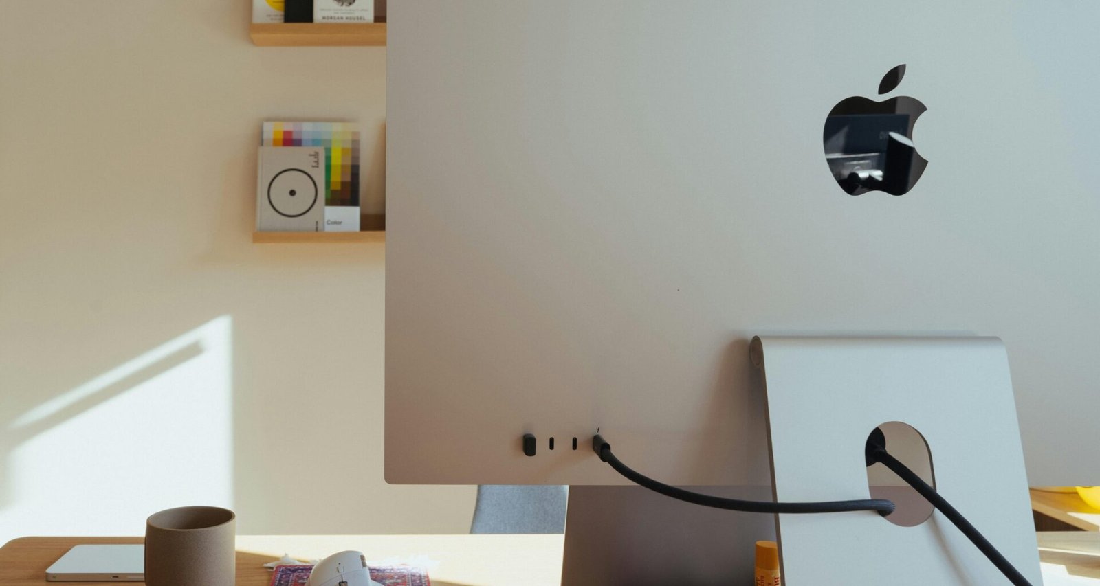 Apple Computer steht auf einem Schreibtisch, dahinter befinden sich Regale mit verschiedenen Gegenständen im Büro.