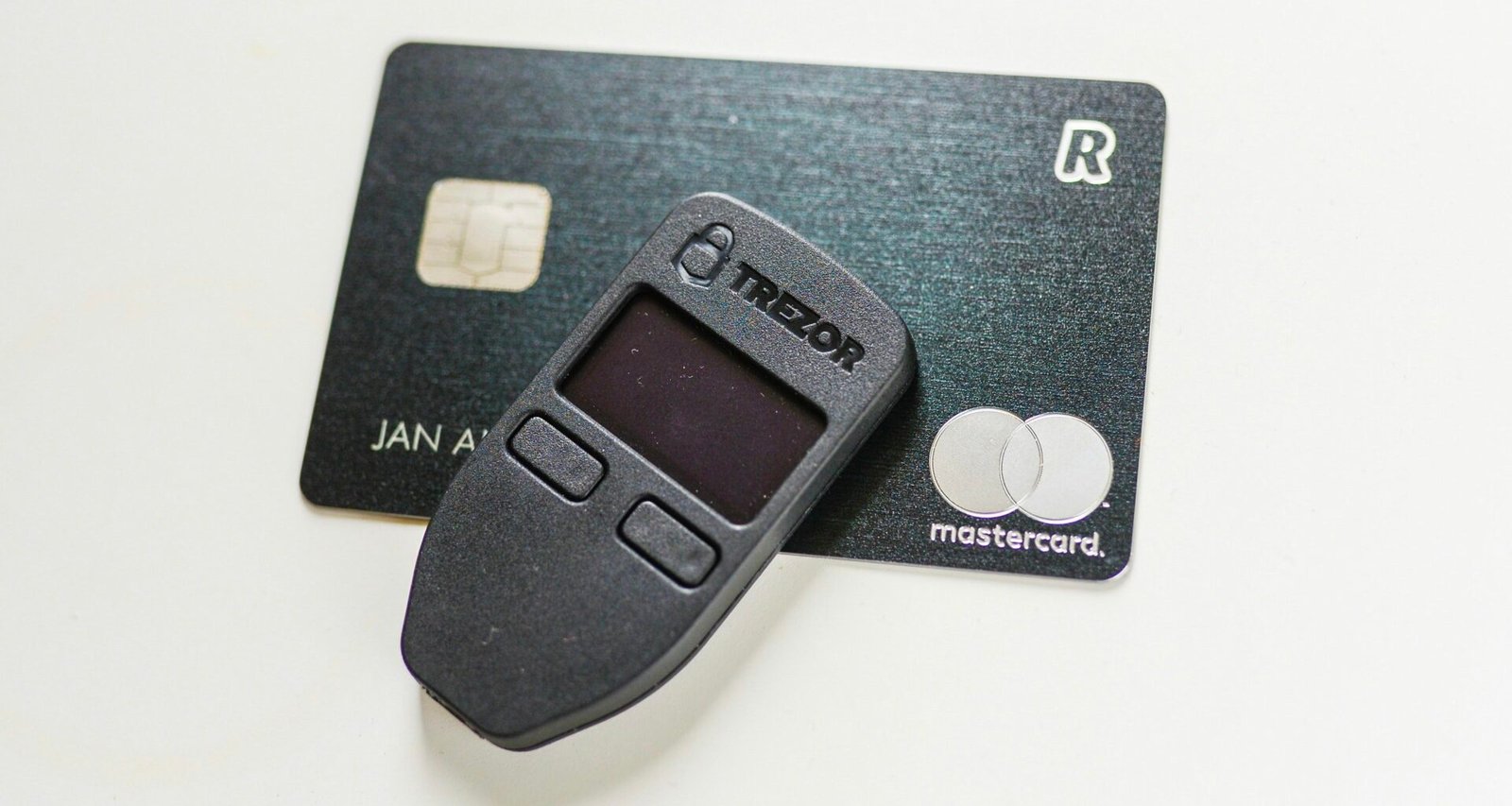 Detailansicht eines ausgeschalteten Trezor-Hardware-Wallets für Kryptowährungen, auf weißem Hintergrund liegend.