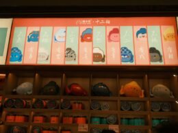 Mehrere Daruma-Puppen und passendes Merchandise werden in einem japanischen Geschäft auf einem Regal nebeneinandergestellt präsentiert.