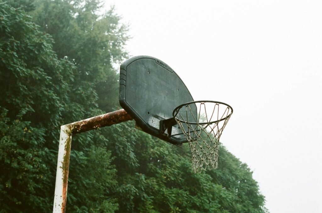 Ein moderner Basketballkorb steht tagsüber unter wolkenlosem, weißem Himmel. Umgebung ohne Menschen.