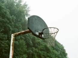 Ein moderner Basketballkorb steht tagsüber unter wolkenlosem, weißem Himmel. Umgebung ohne Menschen.