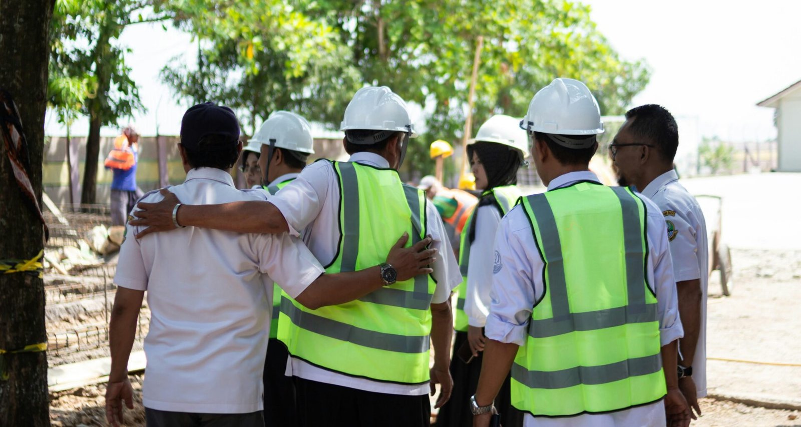 Eine Gruppe Bauarbeiter mit Schutzhelmen und Warnwesten berät sich auf einer Baustelle vor Beginn der Arbeiten.