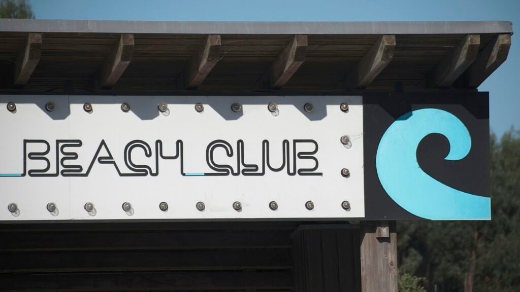 Beach Club Schild mit Wellenlogo vor blauem Himmel, modernes Design für Gastronomie, aufgenommen von Miguel A Amutio