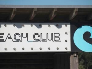 Beach Club Schild mit Wellenlogo vor blauem Himmel, modernes Design für Gastronomie, aufgenommen von Miguel A Amutio