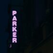 Neonschriftzug Parker leuchtet seitlich an einem Gebäude als modernes Werbeelement bei Nacht