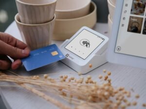 Nahaufnahme einer Hand, die mit einer Kreditkarte an einem Kartenlesegerät am Point of Sale bezahlt.