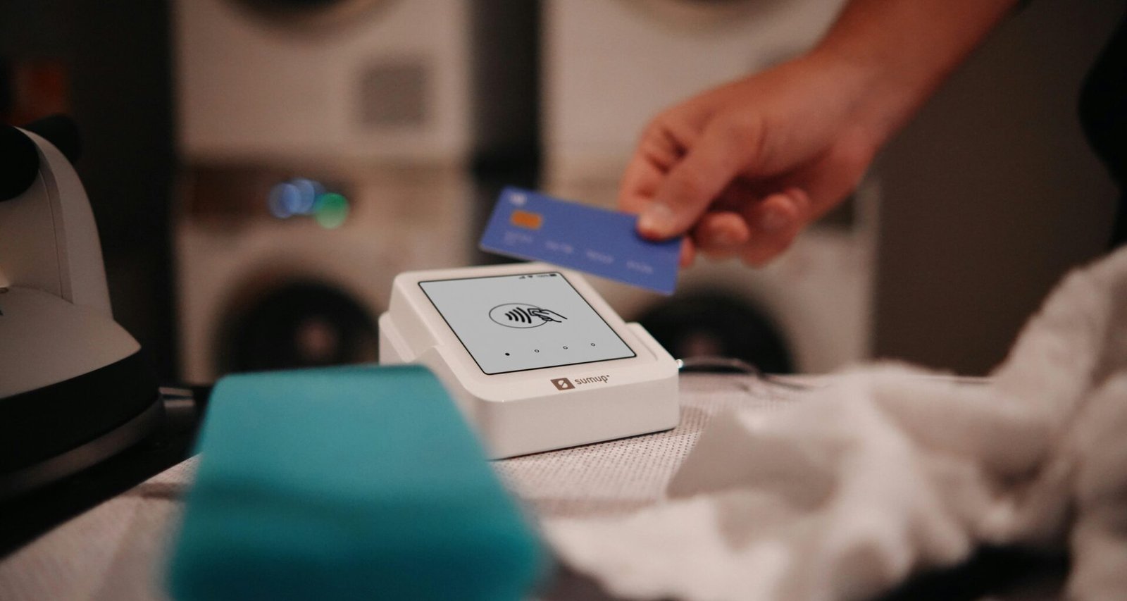 Eine Person bezahlt in einer modernen Wäscherei mit einer Karte an einem elektronischen Bezahlterminal.