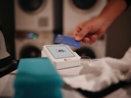 Eine Person bezahlt in einer modernen Wäscherei mit einer Karte an einem elektronischen Bezahlterminal.