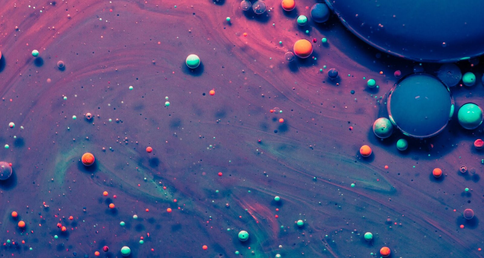 Makroaufnahme von blauen und pinken Wassertröpfchen auf einer glatten Oberfläche, Farbkontrast im Detail sichtbar