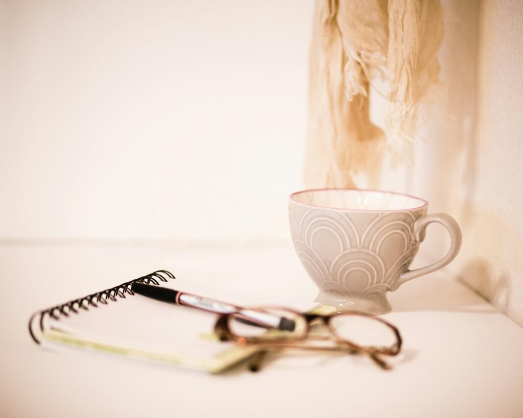 Braun gerahmte Brille liegt neben einer grauen Tasse auf einem hellen Schreibtisch, minimalistisches Büro-Accessoire