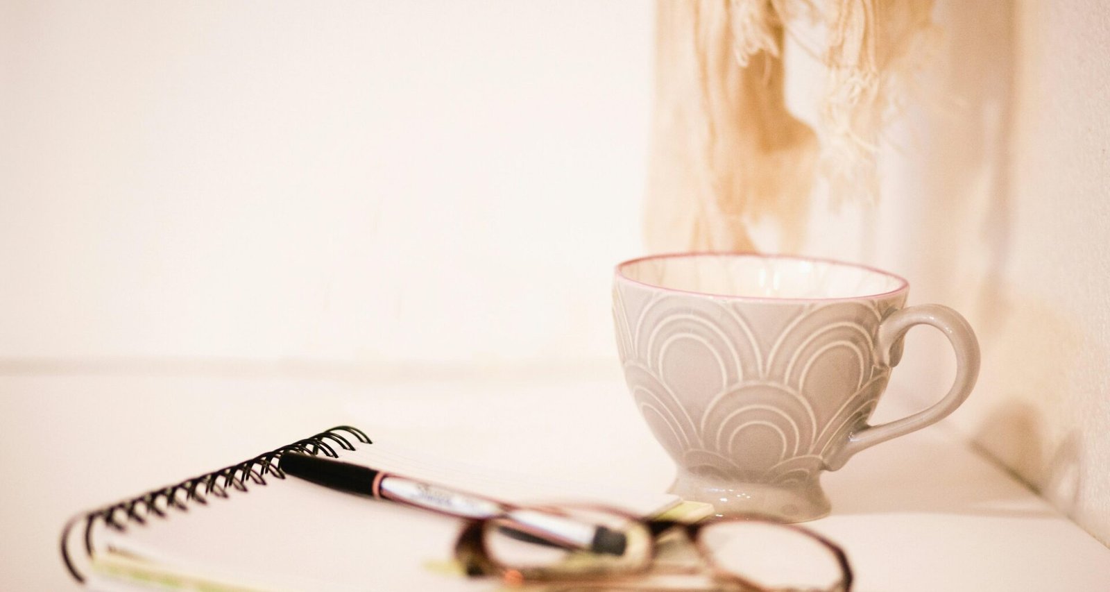 Braune Brillengestelle liegen neben einer grauen Kaffeetasse auf einem hellen Schreibtisch, ideal für Technik- und Bürothemen.