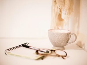 Braune Brillengestelle liegen neben einer grauen Kaffeetasse auf einem hellen Schreibtisch, ideal für Technik- und Bürothemen.