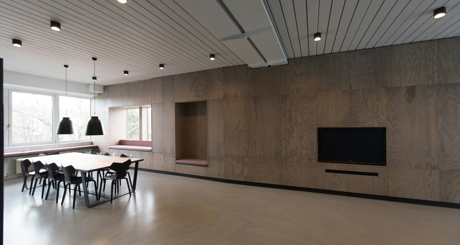 Brauner Holztisch mit Stühlen vor einem großen Fenster in einem modernen Raum mit viel Tageslicht