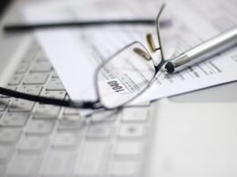 Brille und Stift auf ausgefülltem Steuerformular, daneben ein Laptop, Symbol für digitale Steuerbearbeitung