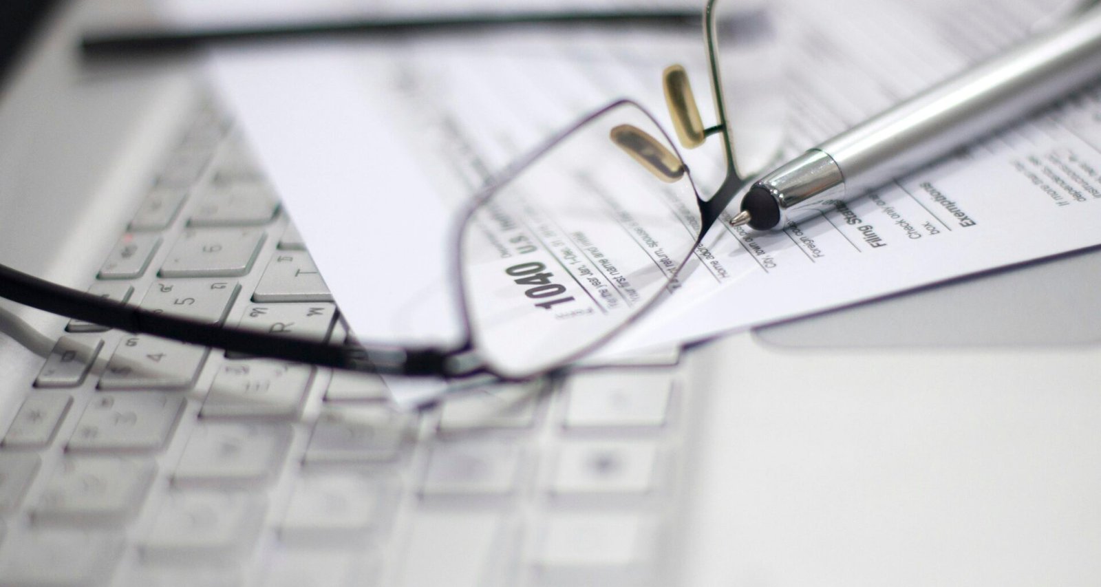 Brille und Stift auf einem Steuerformular neben einem Laptop – Symbol für digitale Finanzverwaltung
