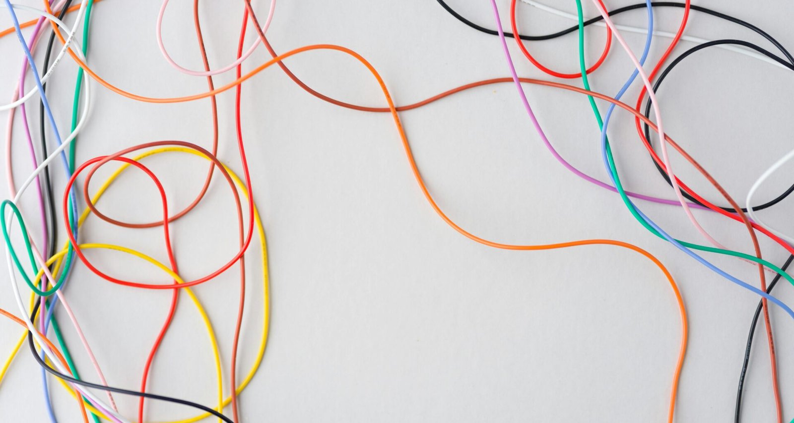 Mehrere bunte Kabel sind auf einem weißen Hintergrund durcheinandergelegt und repräsentieren technische Vernetzung