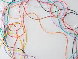 Mehrere bunte Kabel sind auf einem weißen Hintergrund durcheinandergelegt und repräsentieren technische Vernetzung