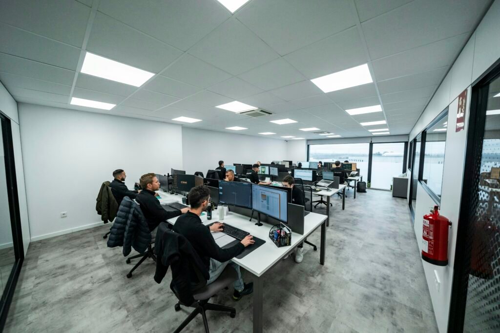 Mehrere Büroangestellte sitzen an Schreibtischen und arbeiten konzentriert an Computern in einer modernen Büroumgebung.