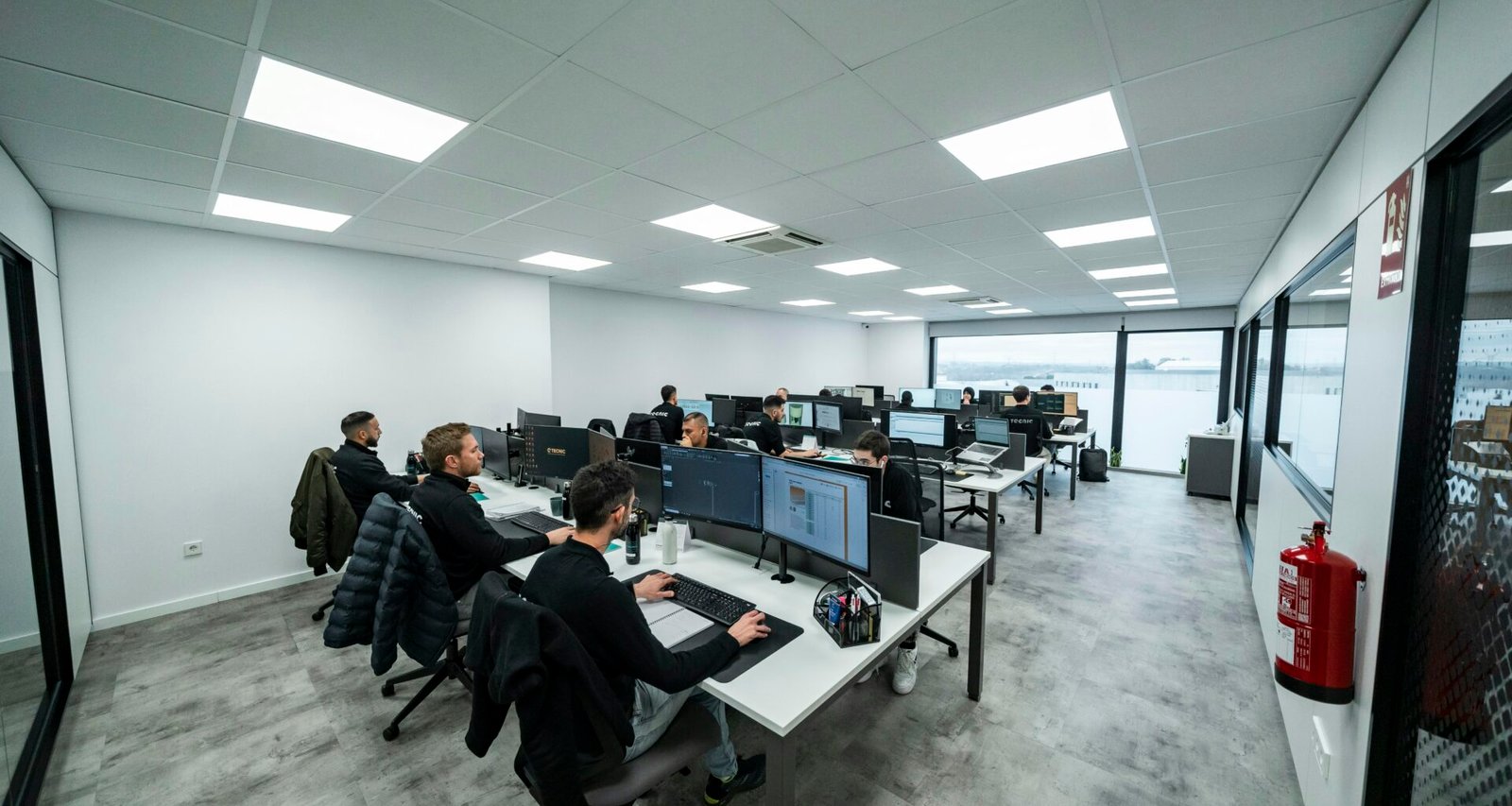 Mehrere Büroangestellte sitzen an Schreibtischen und arbeiten konzentriert an Computern in einer modernen Büroumgebung.