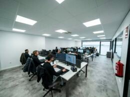 Mehrere Büroangestellte sitzen an Schreibtischen und arbeiten konzentriert an Computern in einer modernen Büroumgebung.