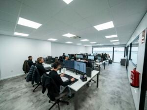 Mehrere Büroangestellte sitzen an Schreibtischen und arbeiten konzentriert an Computern in einer modernen Büroumgebung.