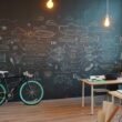 Bürofläche mit großer Kreidetafel, künstlerischer Wandgestaltung und einem Fahrrad neben dem Arbeitsplatz