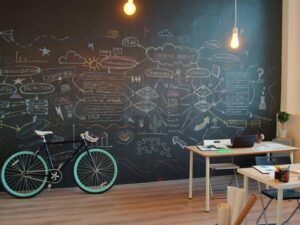 Bürofläche mit großer Kreidetafel, künstlerischer Wandgestaltung und einem Fahrrad neben dem Arbeitsplatz