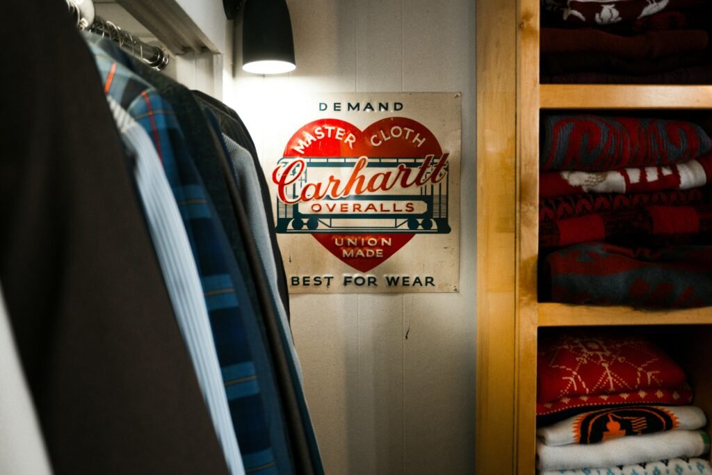 Carhartt Overalls-Schild an einem Bügel in einem Kleiderschrank voller Kleidung und Accessoires