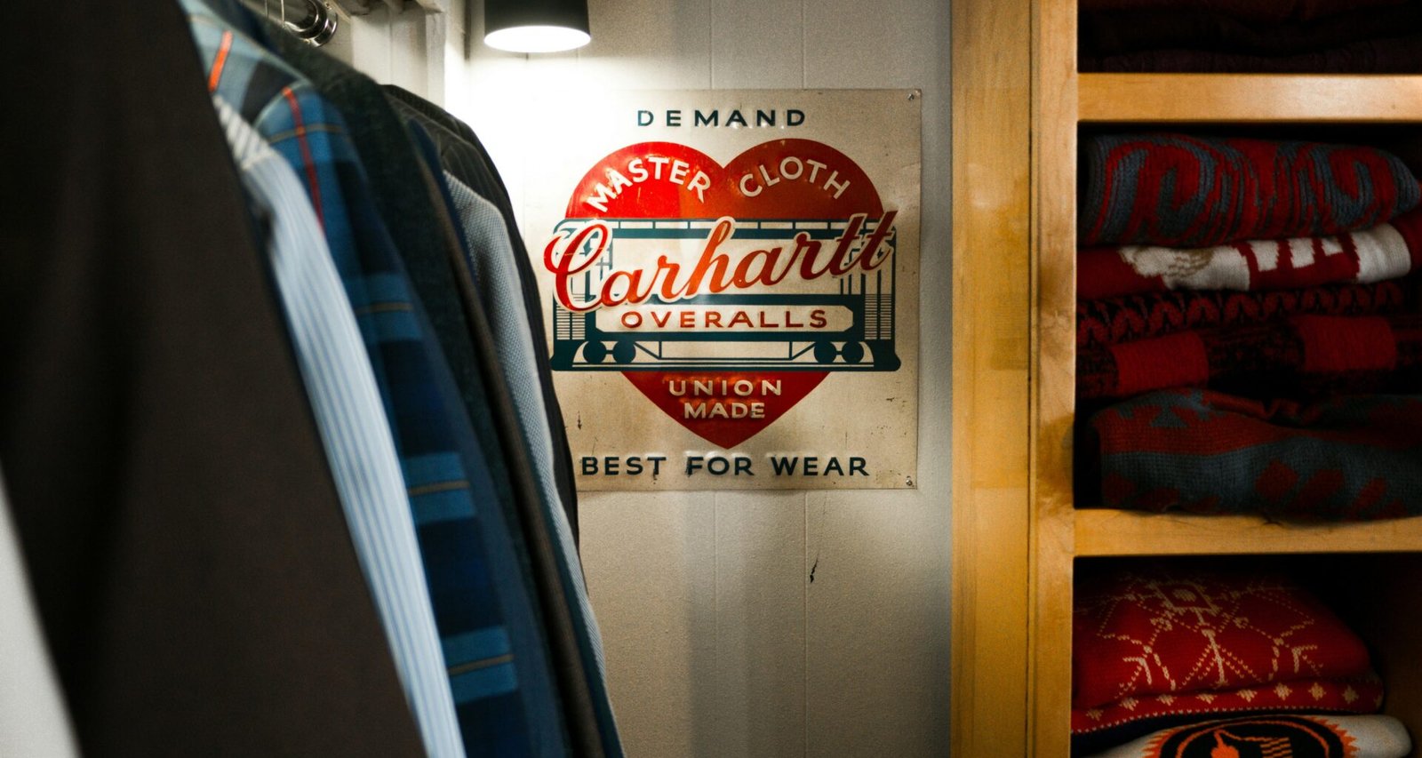 Carhartt Overalls-Schild an einem Bügel in einem Kleiderschrank voller Kleidung und Accessoires