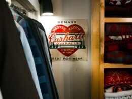 Carhartt Overalls-Schild an einem Bügel in einem Kleiderschrank voller Kleidung und Accessoires