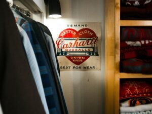 Carhartt Overalls-Schild an einem Bügel in einem Kleiderschrank voller Kleidung und Accessoires