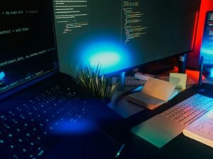 Computerbildschirme mit angezeigtem Programmiercode, umgeben von Neonbeleuchtung in dunkler Umgebung