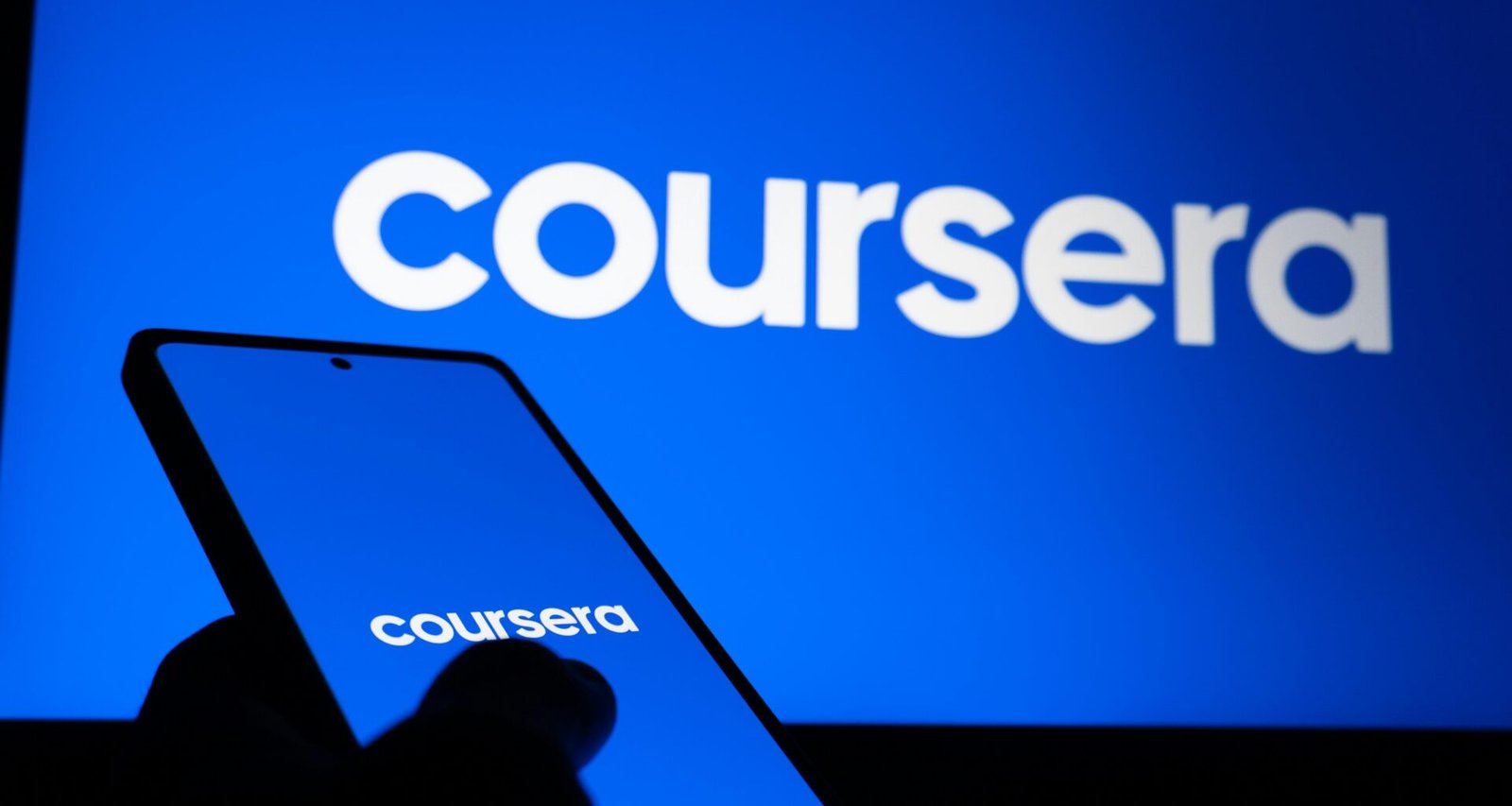 Smartphone zeigt das Coursera Logo, während gleichzeitig das Coursera-Logo auf einem großen Bildschirm zu sehen ist.
