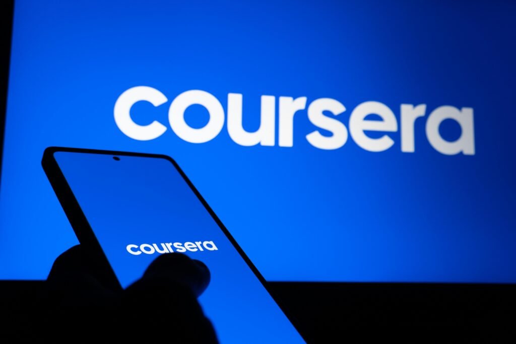 Coursera Logo ist deutlich auf einem Smartphone-Display und einem Computerbildschirm zu sehen, Symbol für digitales Lernen.