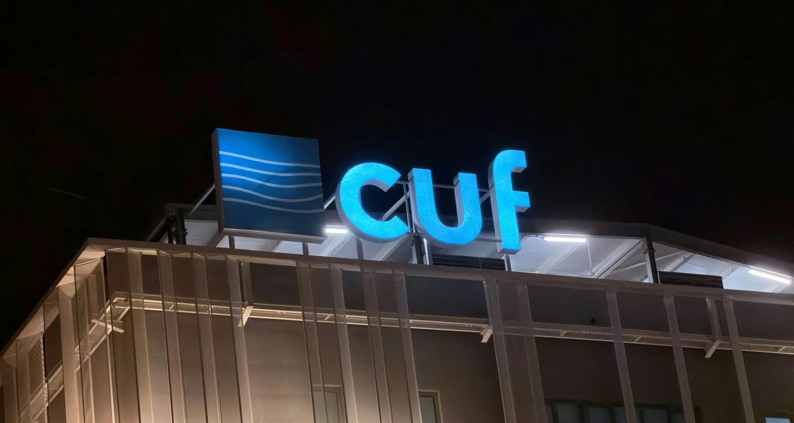 Beleuchtetes Cuf Logo bei Nacht an einer modernen Gebäudefassade mit dunklem Hintergrund.