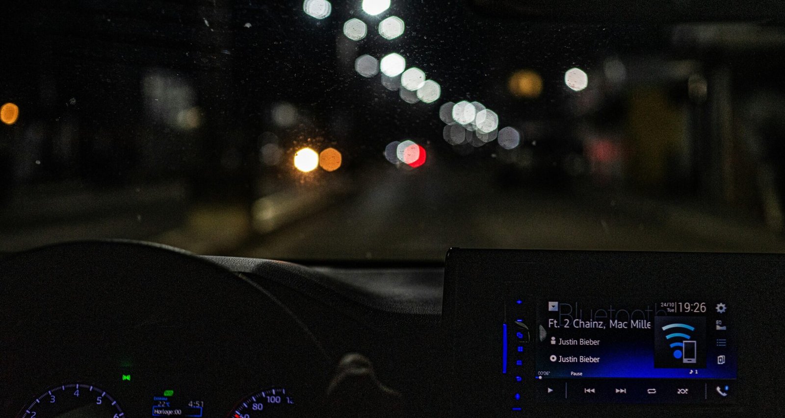 Beleuchtetes Armaturenbrett eines Autos bei nächtlicher Fahrt, mit Fokus auf Anzeigen und Tachometer.