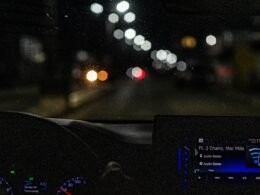 Beleuchtetes Armaturenbrett eines Autos bei nächtlicher Fahrt, mit Fokus auf Anzeigen und Tachometer.