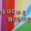 Das Wort 'true colors' ist mit Scrabble-Buchstaben auf einer hellen Oberfläche ausgelegt