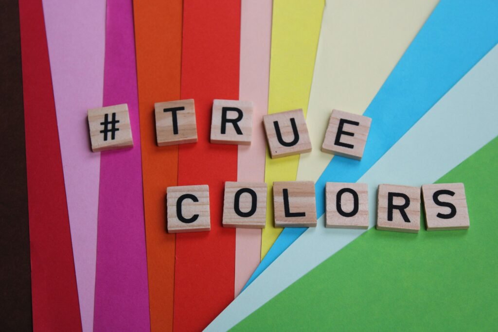 Mehrere Scrabble-Steine bilden das Wort 'True Colors' auf einer ebenen, hellen Oberfläche